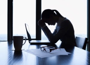 A person dealing with work-related stress sat with their head in hands infront of a laptop